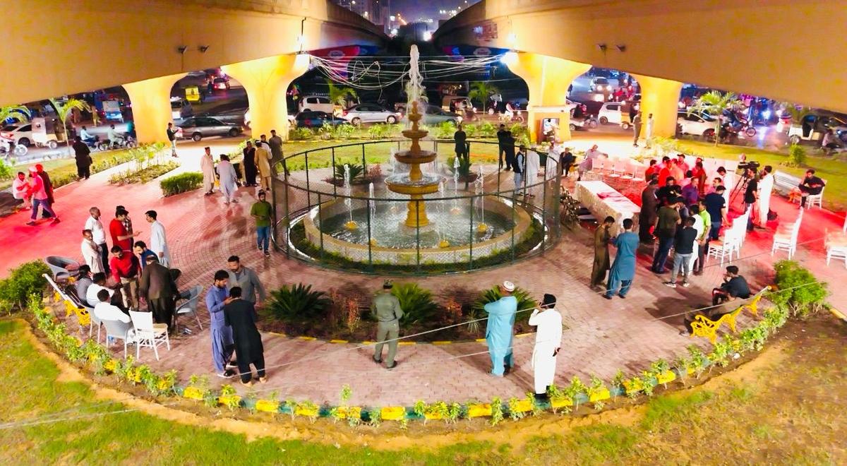 Landscaped fountain park beneath a flyover, seen from above